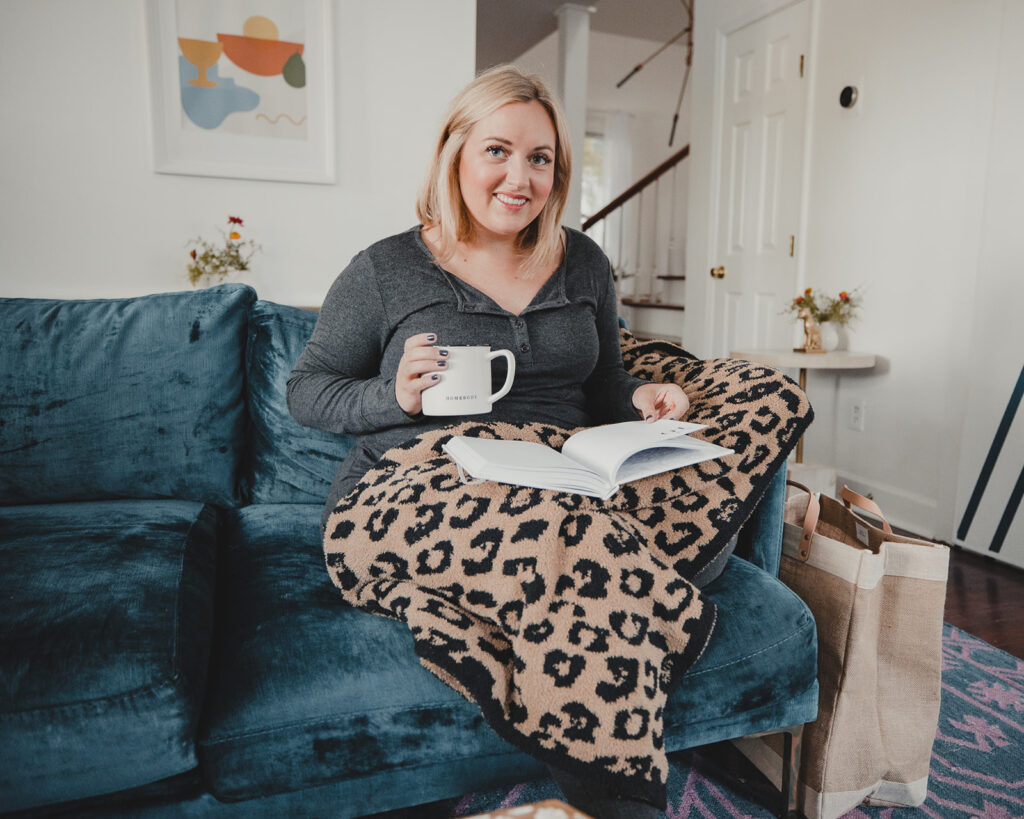 Woman sitting on couch reading, with Barefoot Dreams Leopard Blanket