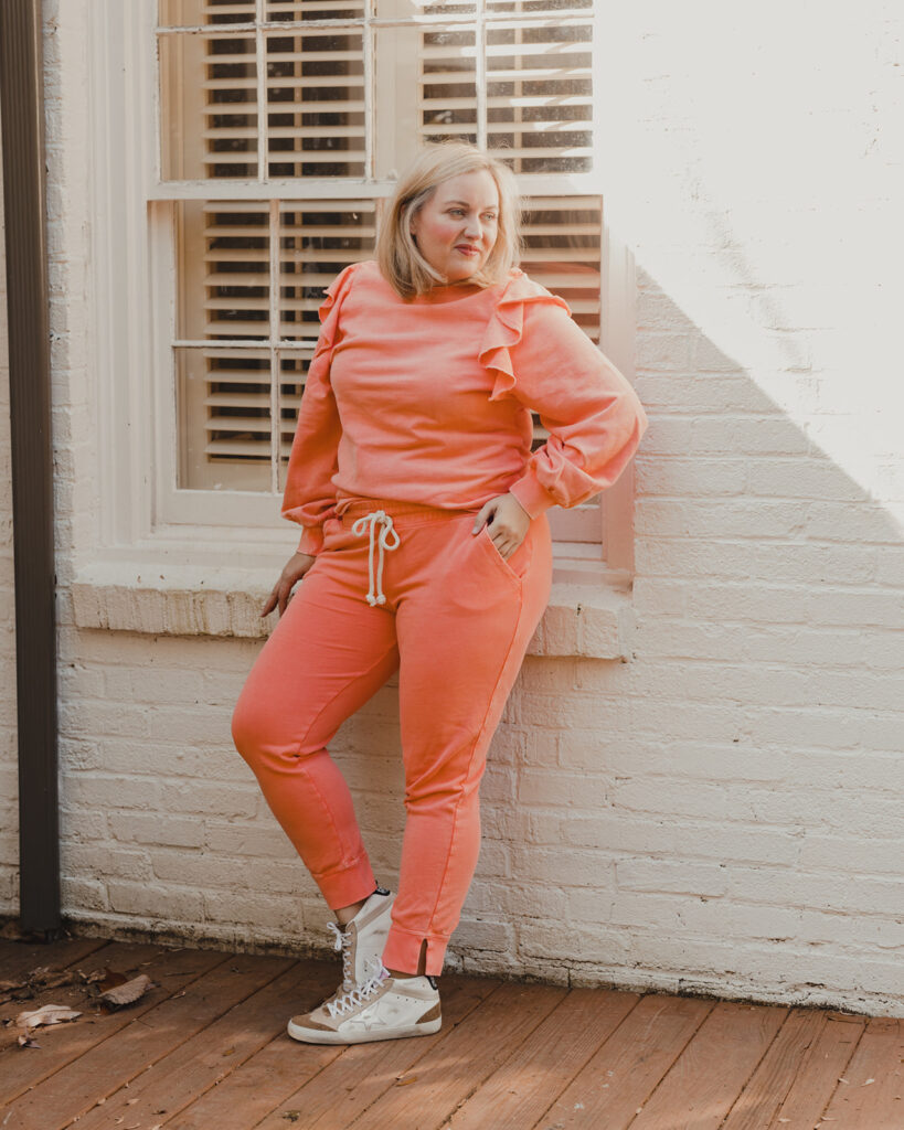 Spring Target Finds - Woman standing in front of white brick house wearing a pinkish peach ruffle sleeve sweater and matching jogger pants with sneakers