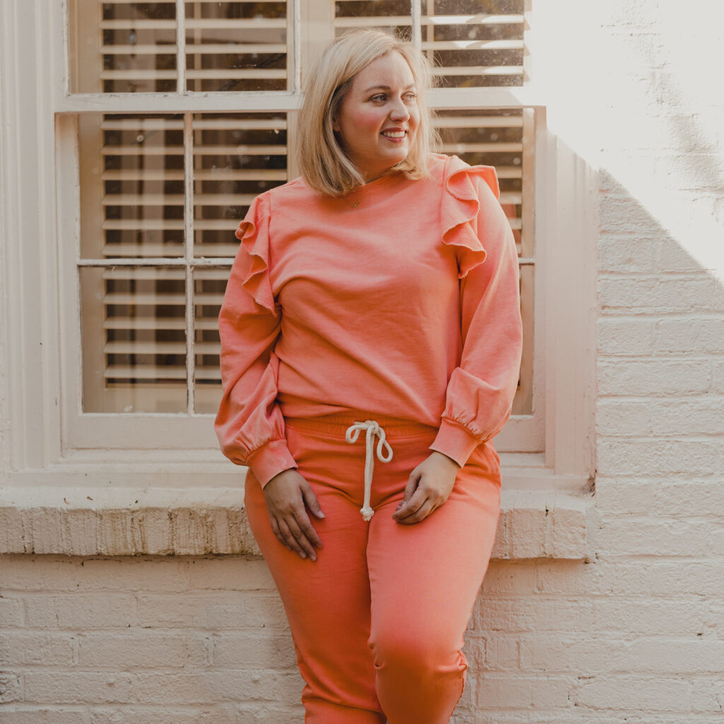 Spring Target Finds - Woman standing in front of white brick house wearing a pinkish peach ruffle sleeve sweater and matching jogger pants