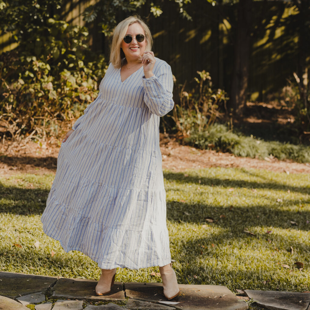 Spring Target Finds - Woman swirling in front of a tree wearing a white and blue striped tiered dress and sunglasses and tan booties