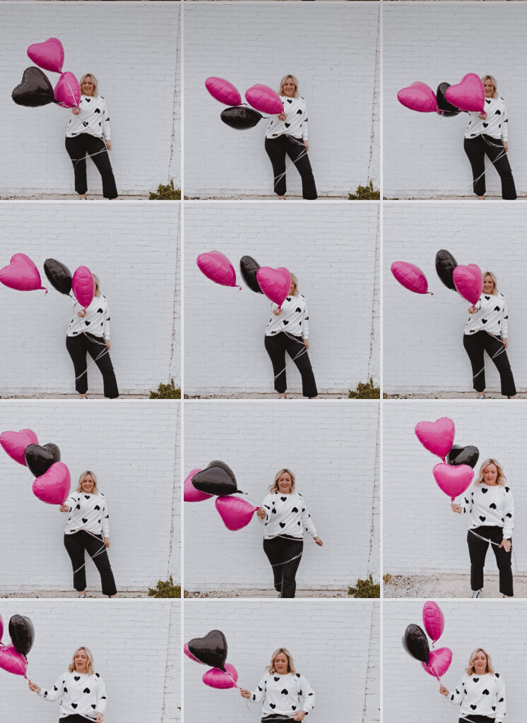 Valentine's Inspired Looks. Woman standing in front of white brick wall holding heart balloons wearing white sweater with hearts, black pants. 