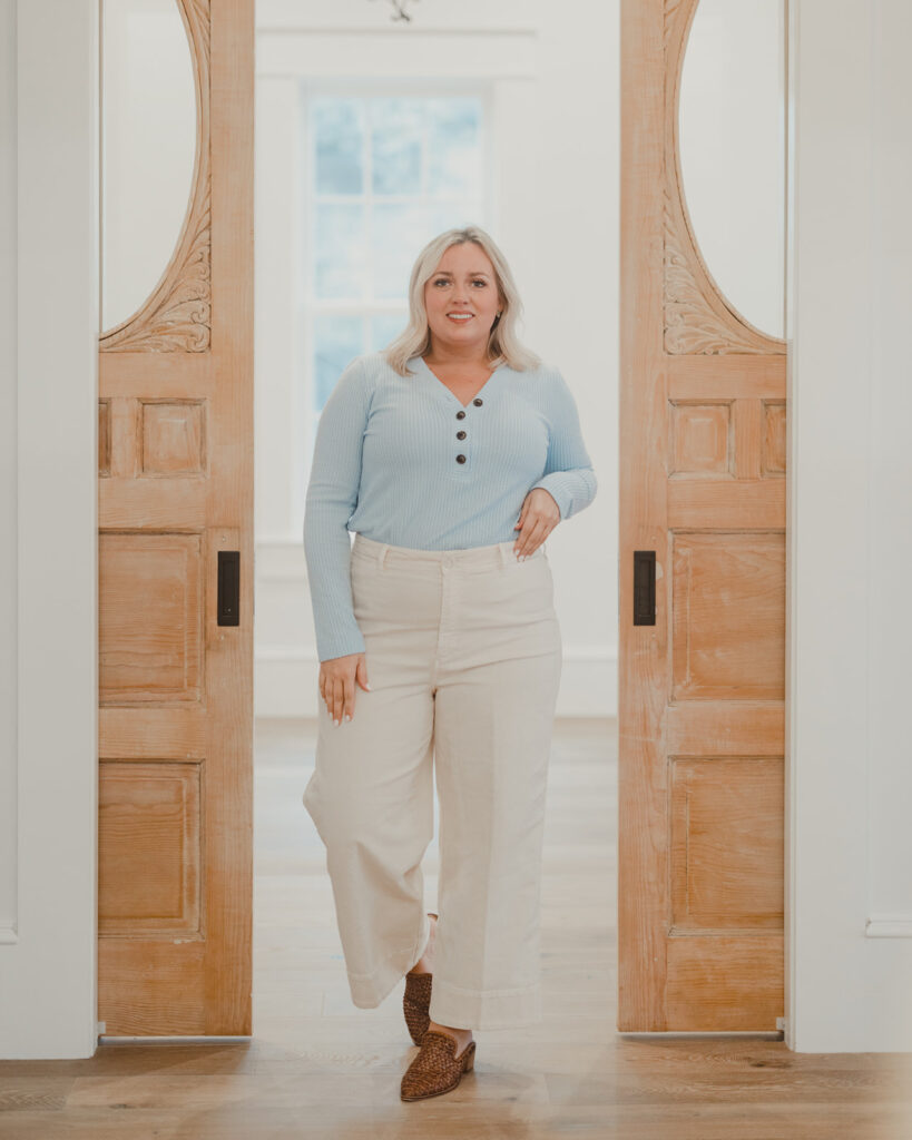 4 Ways To Style Wide Leg Pants woman standing in between pocket doors wearing cream wide leg pants and light blue pastel button up shirt with woven mules