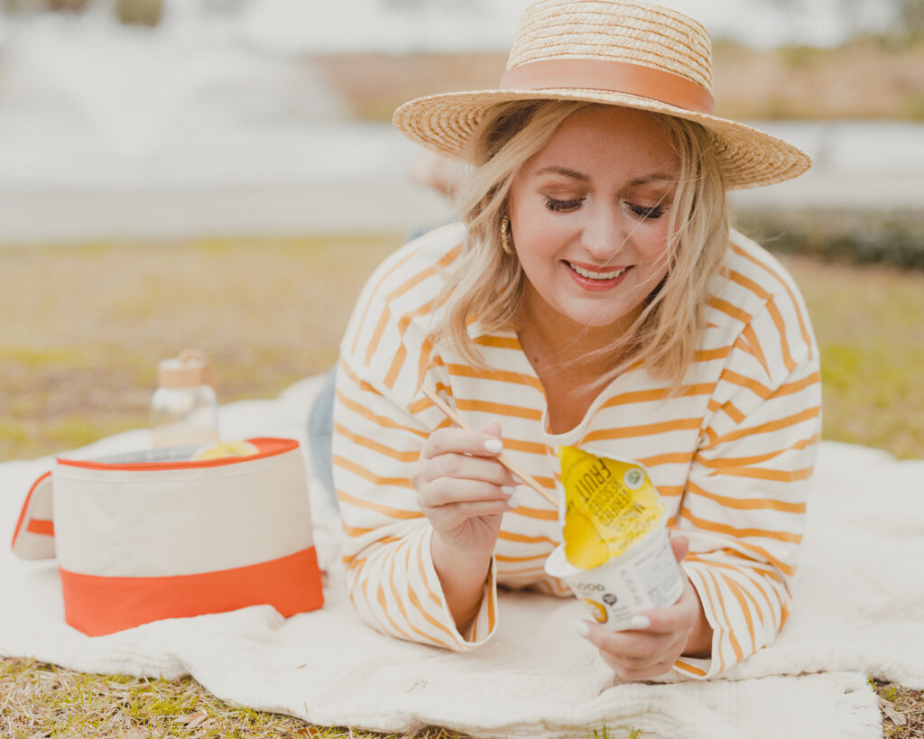 Two Good Yogurt - woman outside in hat having a picnic with Two Good Good Save Lemon flavored Greek Yogurt