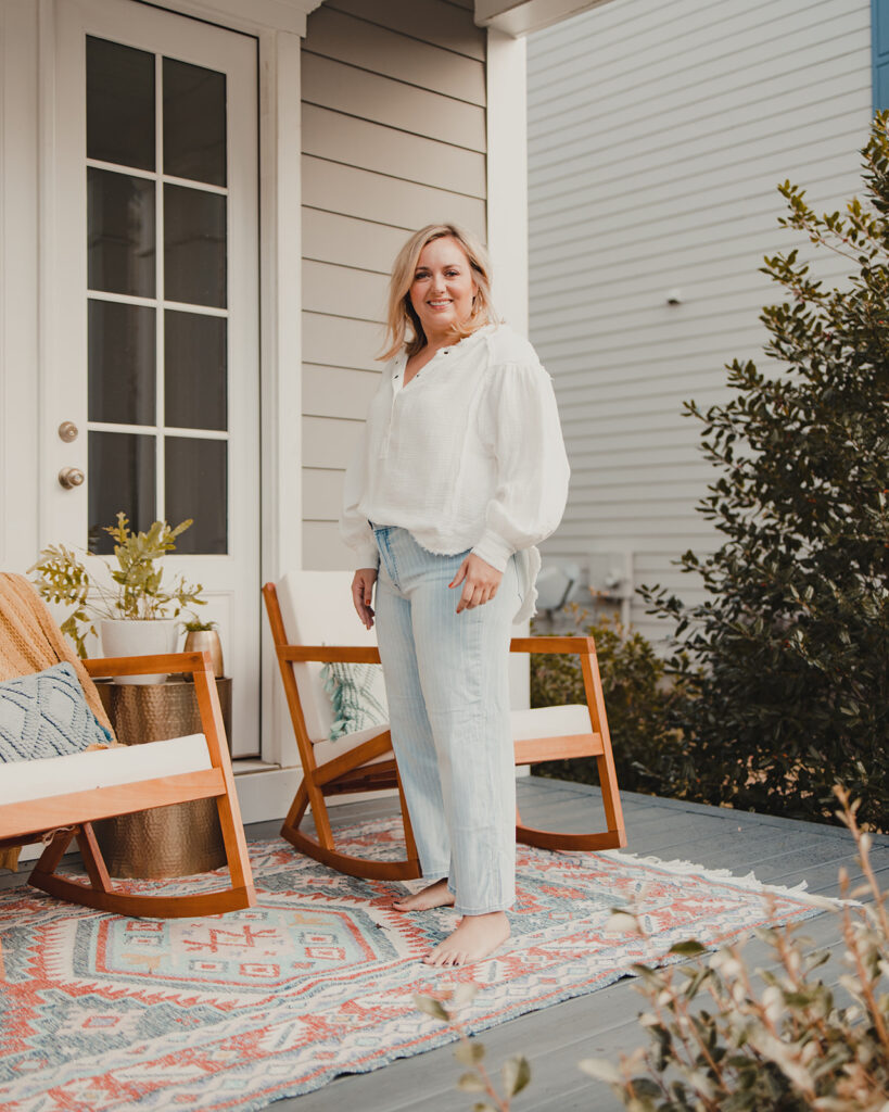 4 Ways To Style Wide Leg Pants woman standing on porch wearing denim wide leg jeans with white gauze top