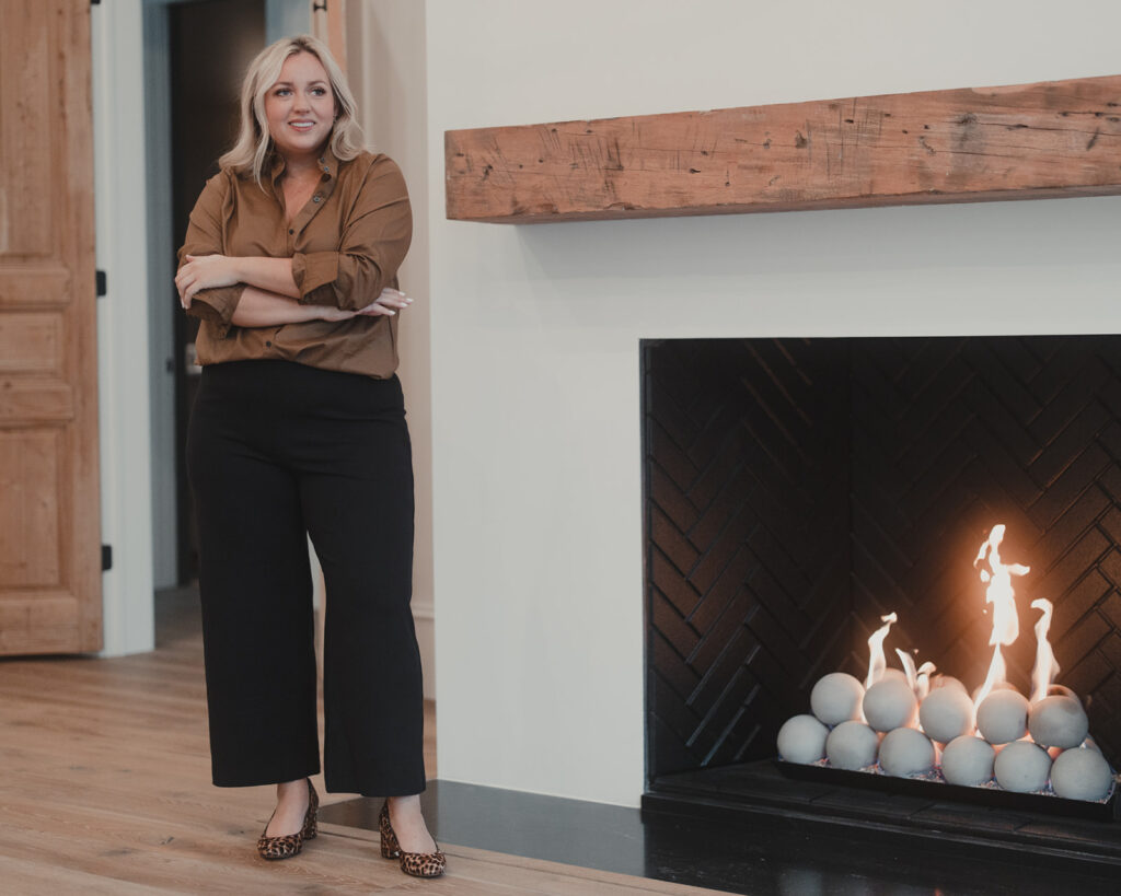 4 Ways To Style Wide Leg Pants woman standing beside fireplace wearing Black Wide Leg Pants with Brown button up shirt
